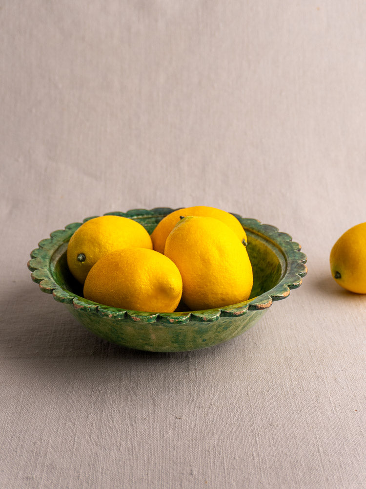 Antique French earthenware bowl with Provençal green glaze, holding lemons, on a light fabric surface.