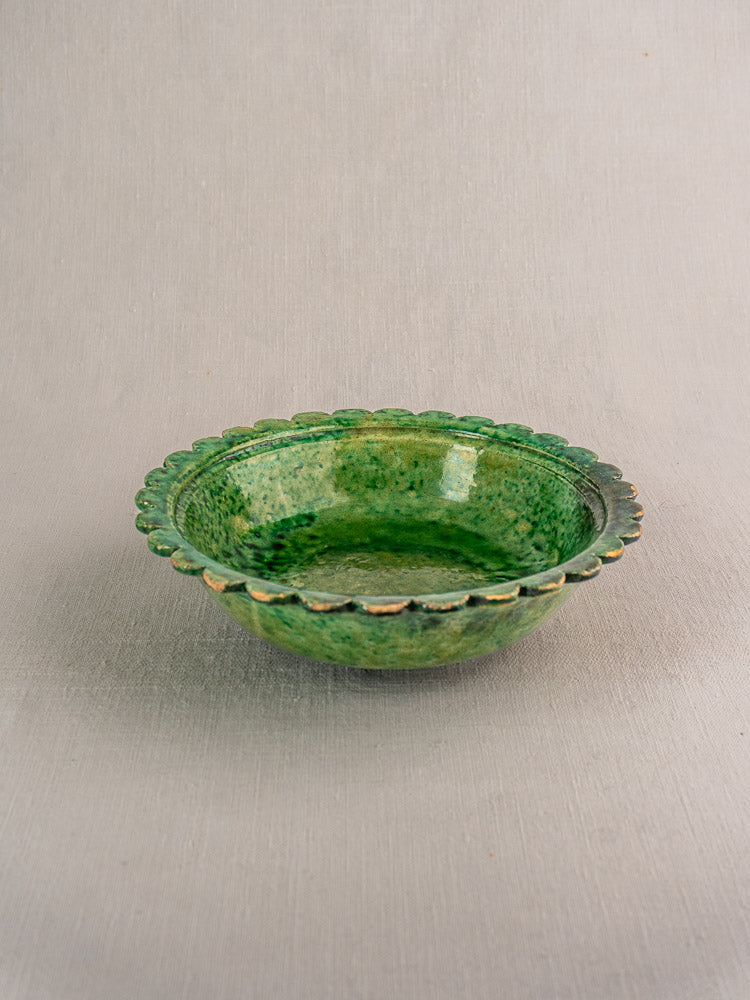 Antique French earthenware bowl with Provençal green glaze, scalloped edge, on a neutral textured surface.