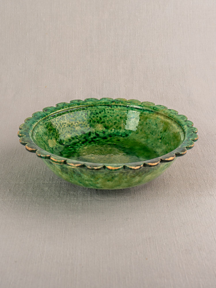 Antique French earthenware bowl with Provençal green glaze, scalloped edge, and mottled finish on light gray textured surface.
