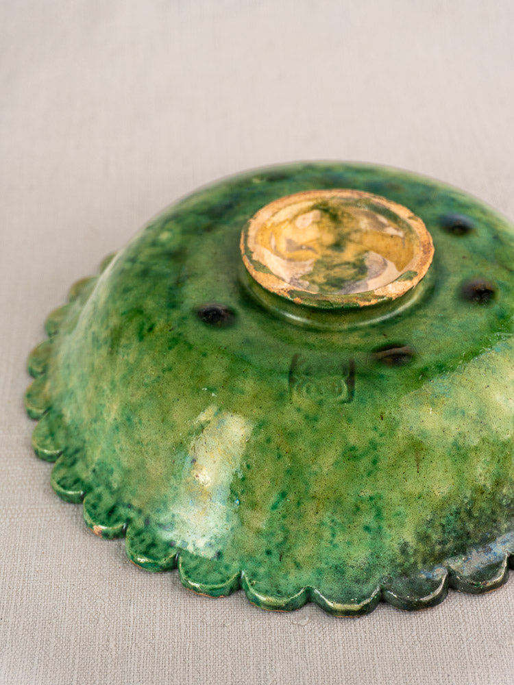 Antique French earthenware bowl with Provençal green glaze, unglazed base visible on neutral fabric background.