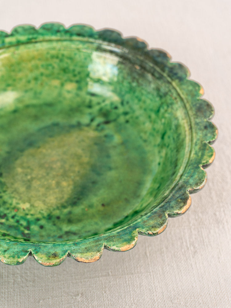 Antique French earthenware bowl with scalloped edge, mottled green and yellow glaze, on light fabric background.