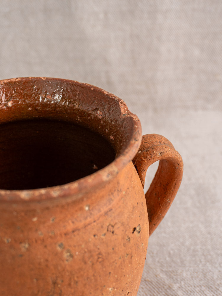 Antique French terracotta pitcher with pinched spout, single handle, and textured weathered surface.