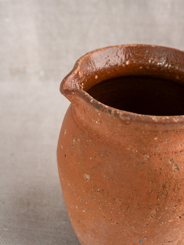 Antique French terracotta pitcher with pinched pouring lip, mid to late 19th century, on a neutral textured background.