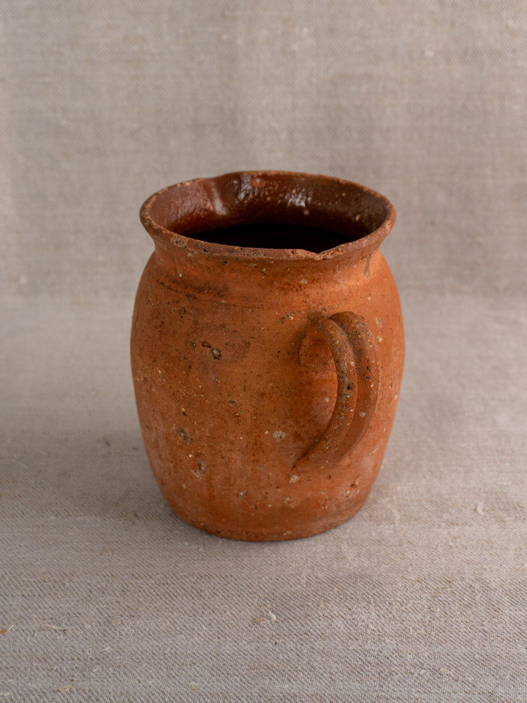Antique French terracotta pitcher with pinched spout and handmade details on textured fabric, farmhouse style.