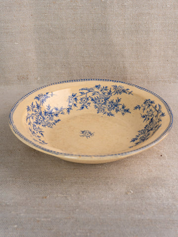 Antique French faience saladier with blue floral rim on cream ceramic, set on beige fabric.