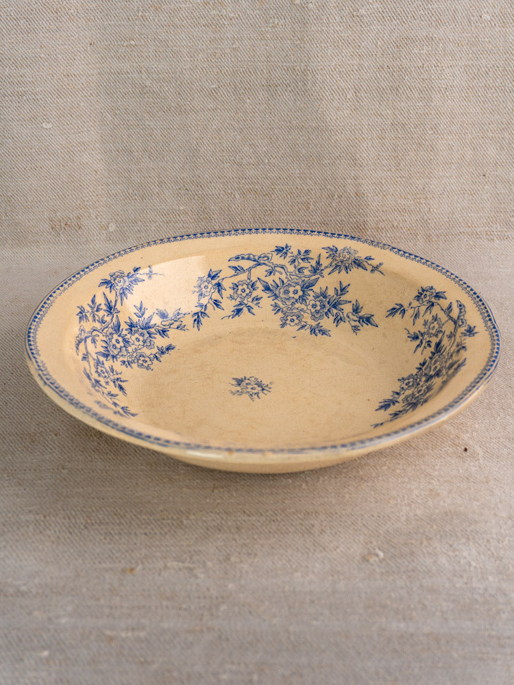 Antique French faience saladier with blue floral rim on cream ceramic, set on beige fabric.