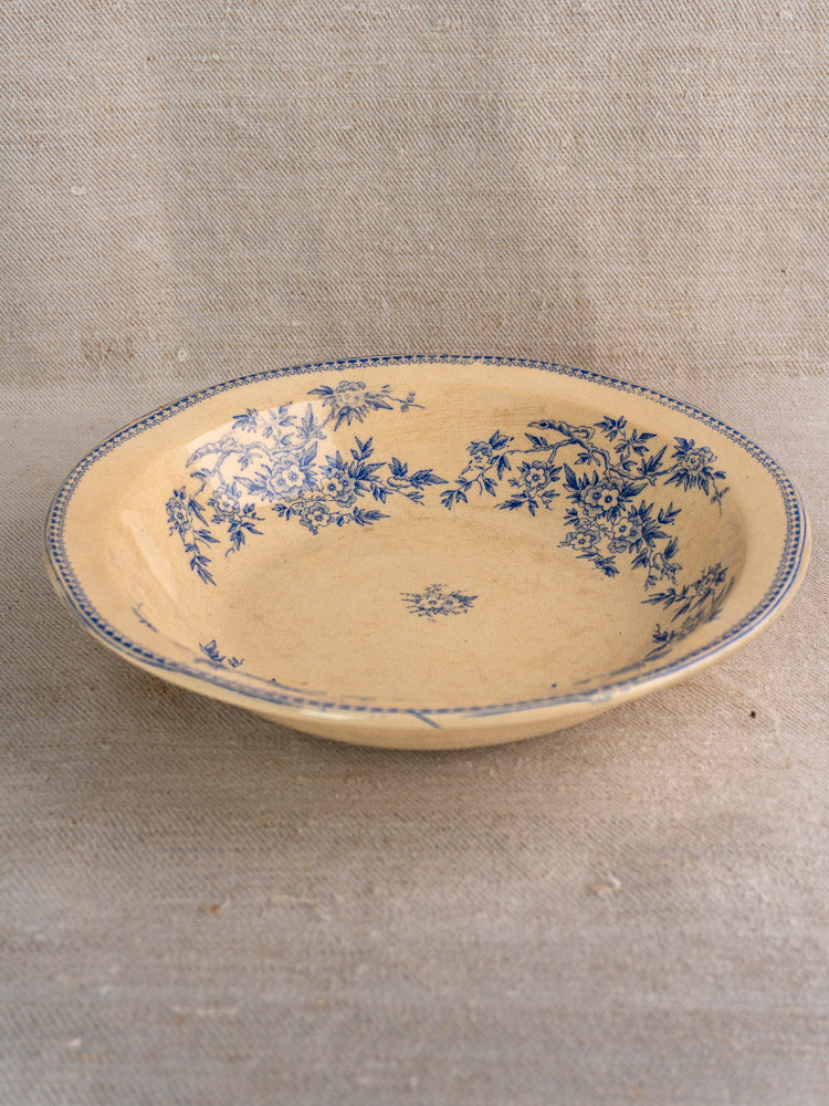 Antique French Grigny Terre de Fer saladier with blue floral rim on beige ceramic, set against textured fabric.