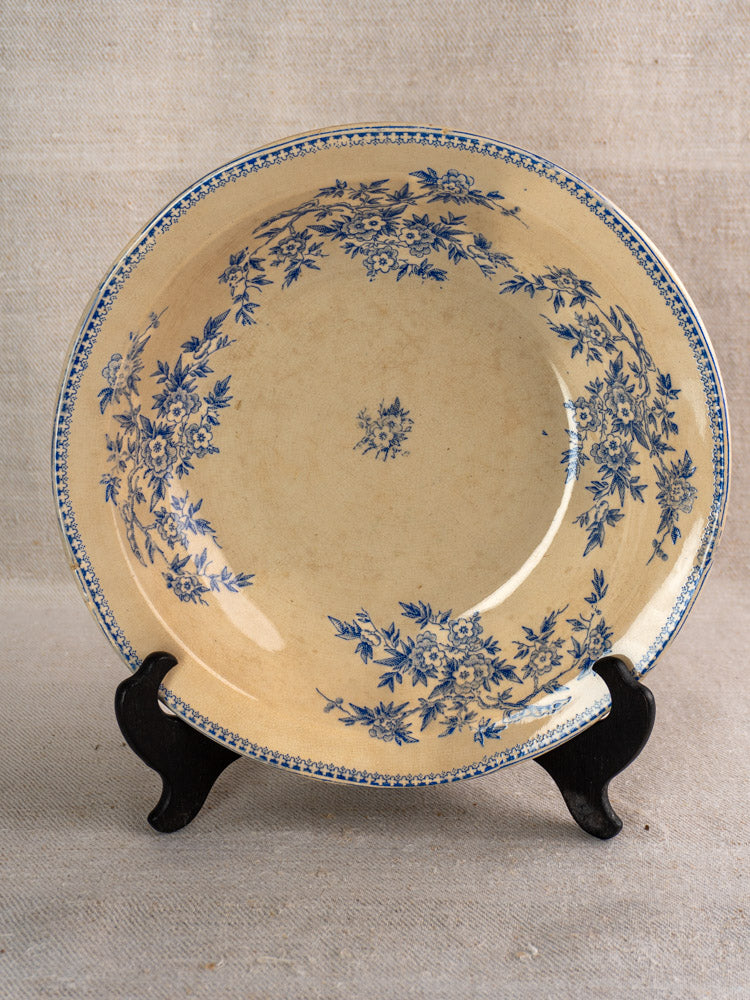 Antique French Grigny Terre de Fer saladier with blue floral transferware on black stand, beige backdrop.