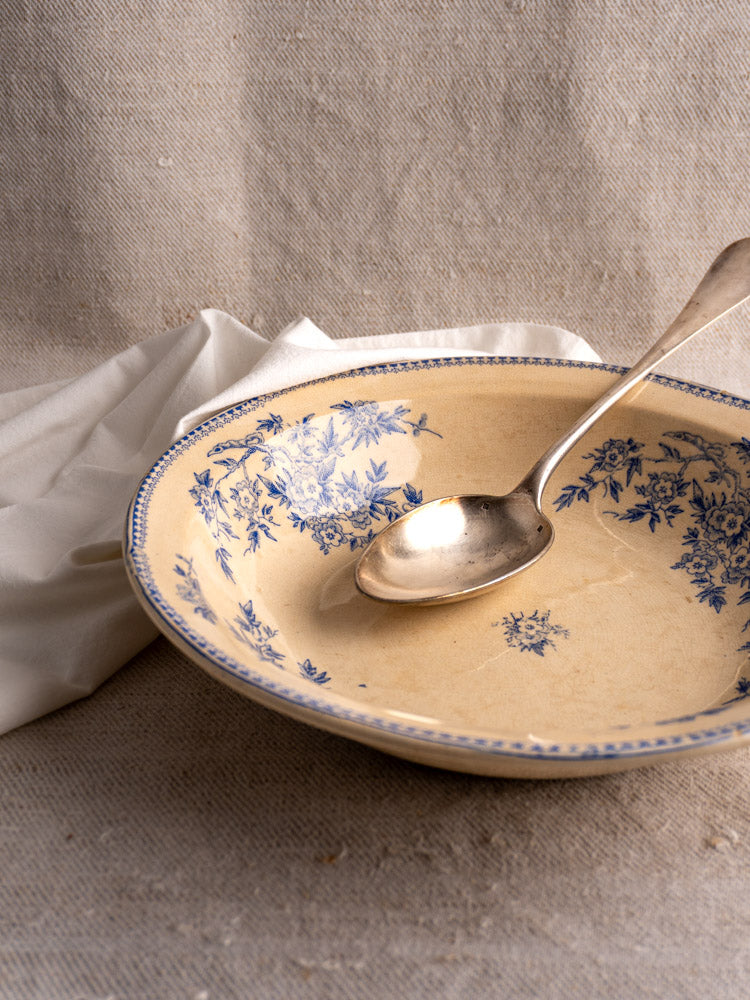 Antique French Grigny Terre de Fer saladier with blue floral transferware and silver spoon on beige surface.