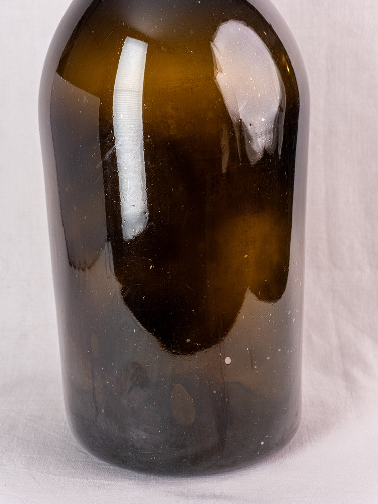 Antique French demijohn in dark olive hand-blown glass with original chain and cork on white fabric.