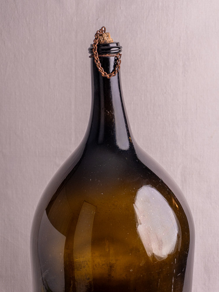 Antique French demijohn in dark olive hand-blown glass with original chain and cork on a light background.