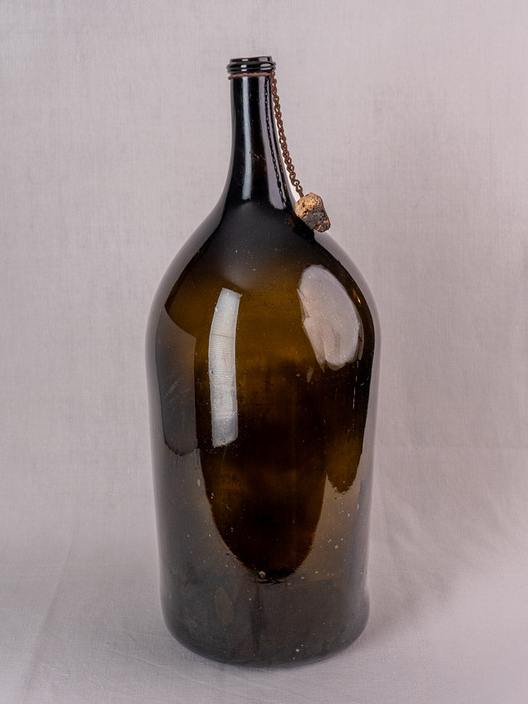 Antique French demijohn in dark olive hand-blown glass with original chain and cork, narrow neck, plain backdrop.