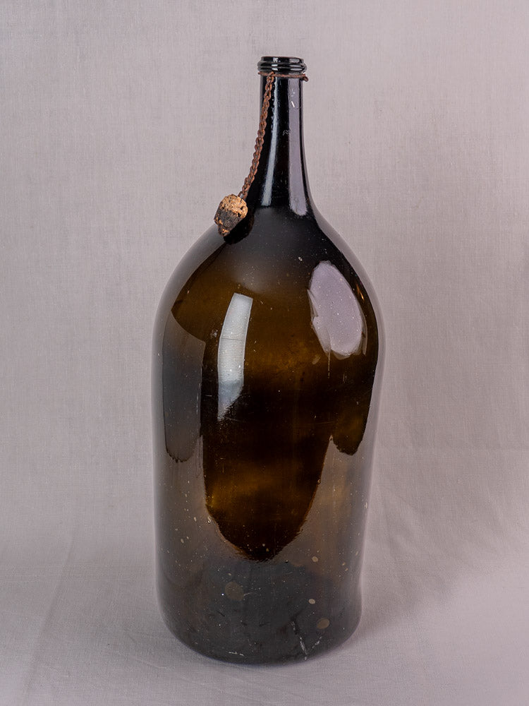 Antique French demijohn in dark olive hand-blown glass with original chain and cork on light gray surface.