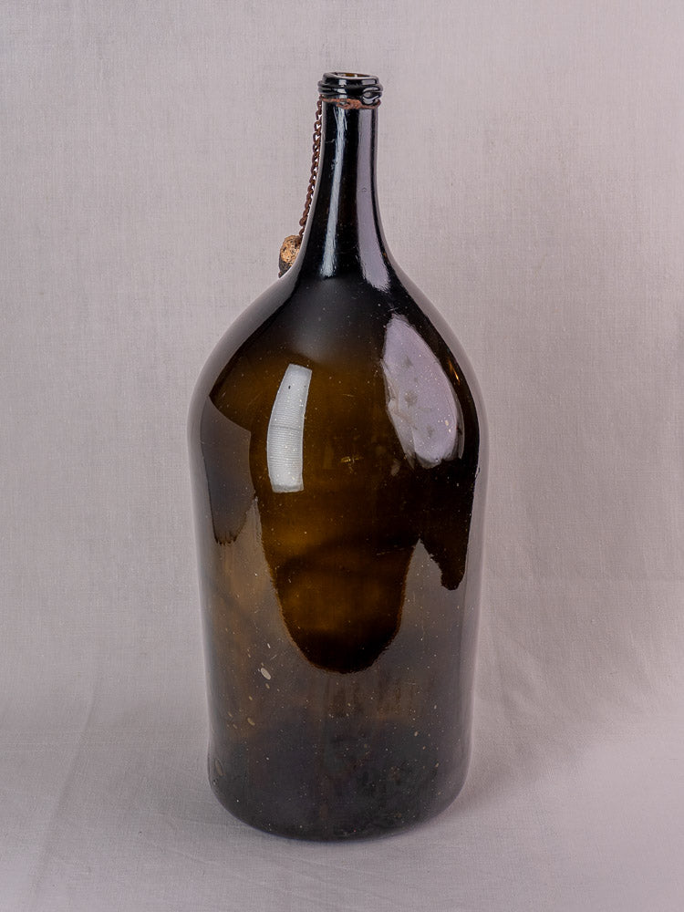 Antique French demijohn in dark olive hand-blown glass with original chain and cork on a light gray surface.