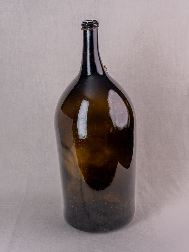 Antique French demijohn in dark olive hand-blown glass with original chain and cork on a light gray background.