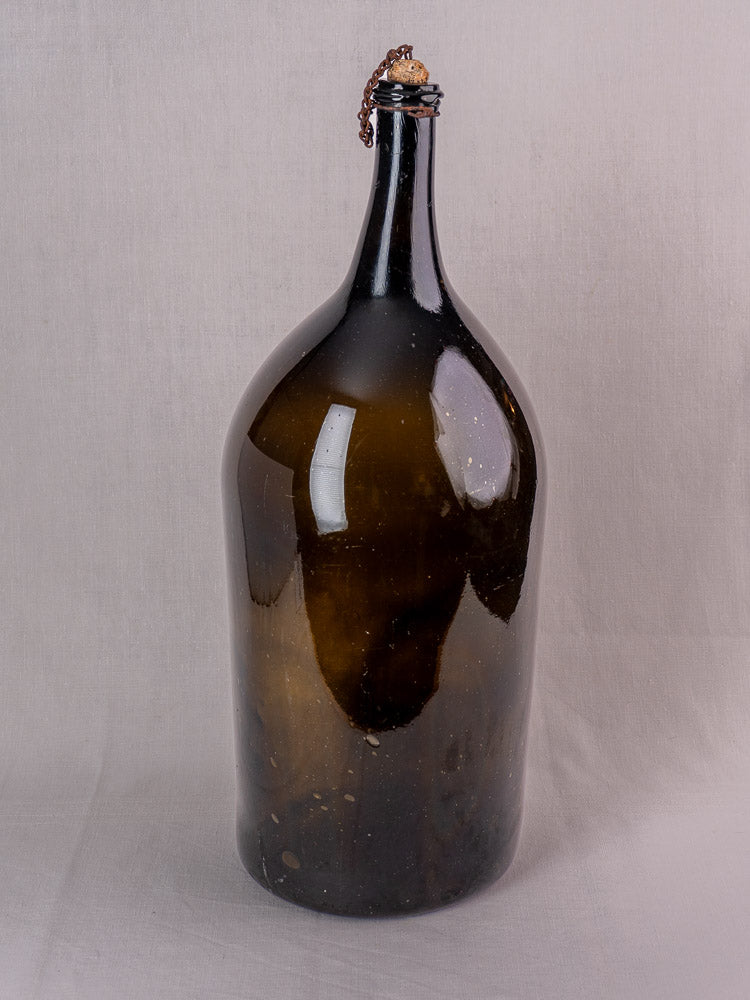 Antique French demijohn in dark olive hand-blown glass with original chain and cork on a light background.
