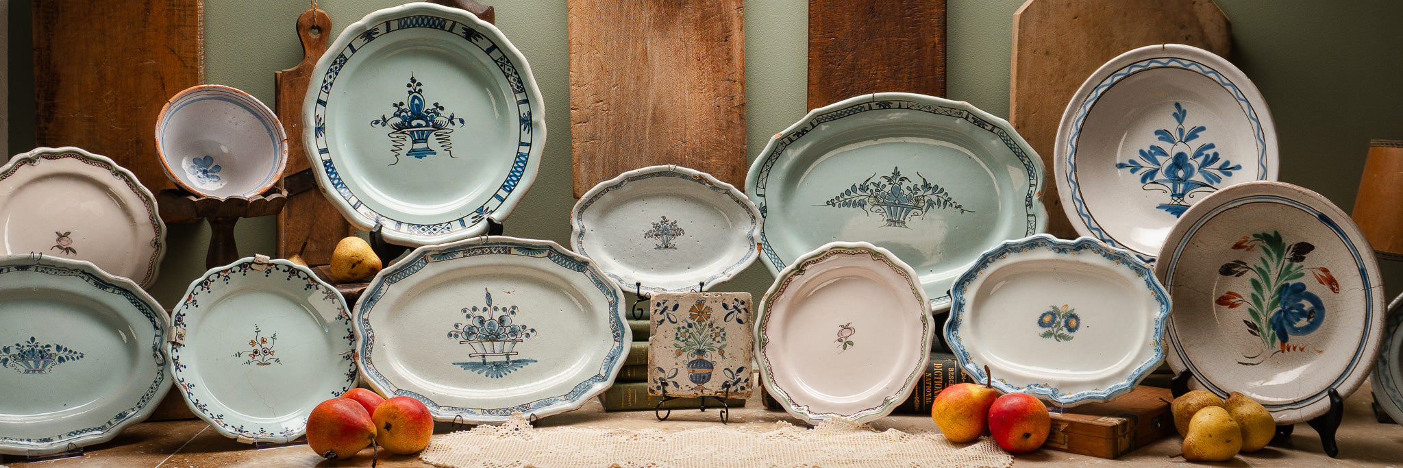 Vintage ceramic plates with floral and pastoral motifs displayed on a table with pears, apples, and wood backdrop.