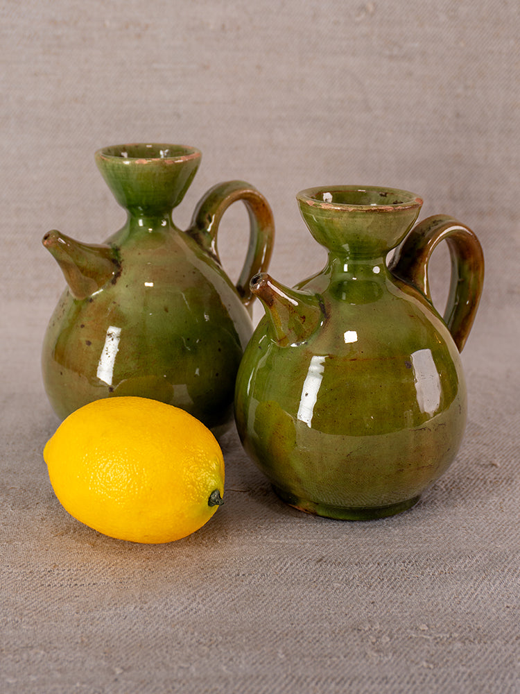 Pair of antique French green glazed earthenware pitchers with lemon on textured beige surface.