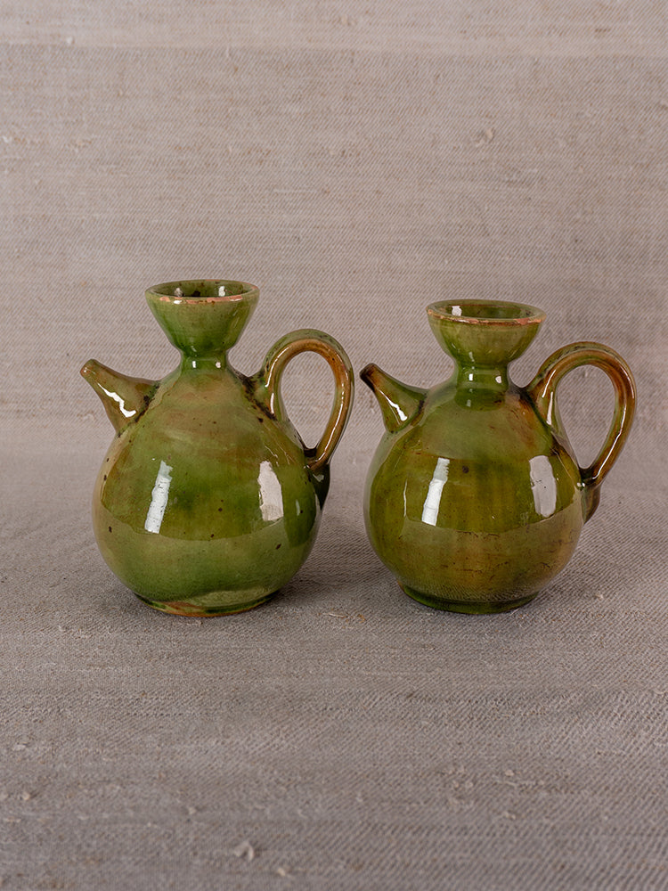 Pair of antique French green glazed earthenware oil and vinegar pichets on beige fabric background.