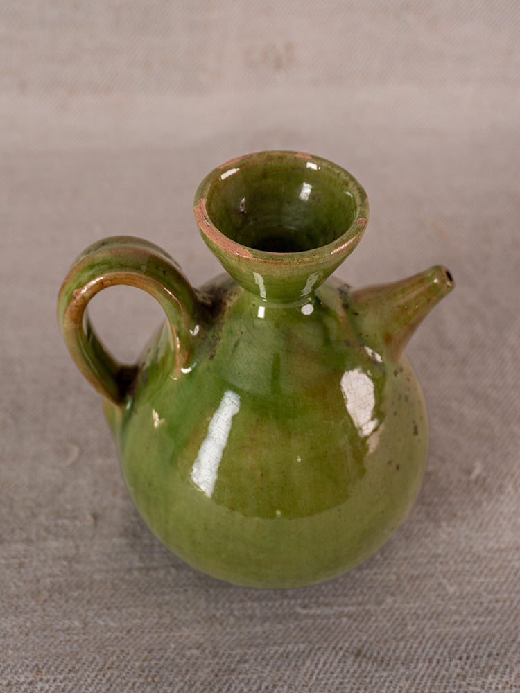 Pair of antique French green glazed earthenware oil and vinegar pichets with handles and spouts on gray textured surface.