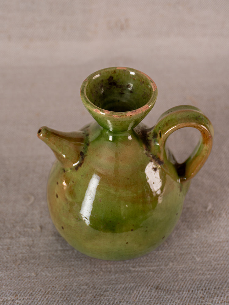 Pair of antique French green glazed earthenware oil and vinegar pichets on beige fabric surface.