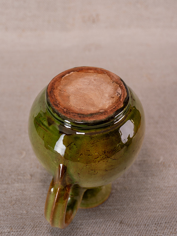 Pair of antique French green-glazed earthenware pitchers, upside down on textured beige fabric.