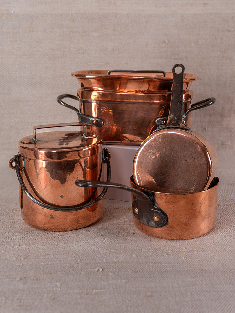Antique French copper apprentice set with lidded pot, large-rimmed pan, and small upright-handled saucepan on beige surface.