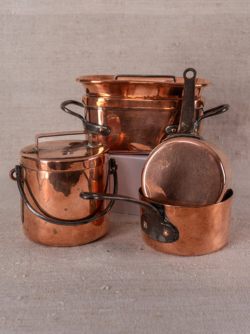 Antique French copper apprentice set with lidded pot, large-rimmed pan, and small upright-handled saucepan on beige surface.