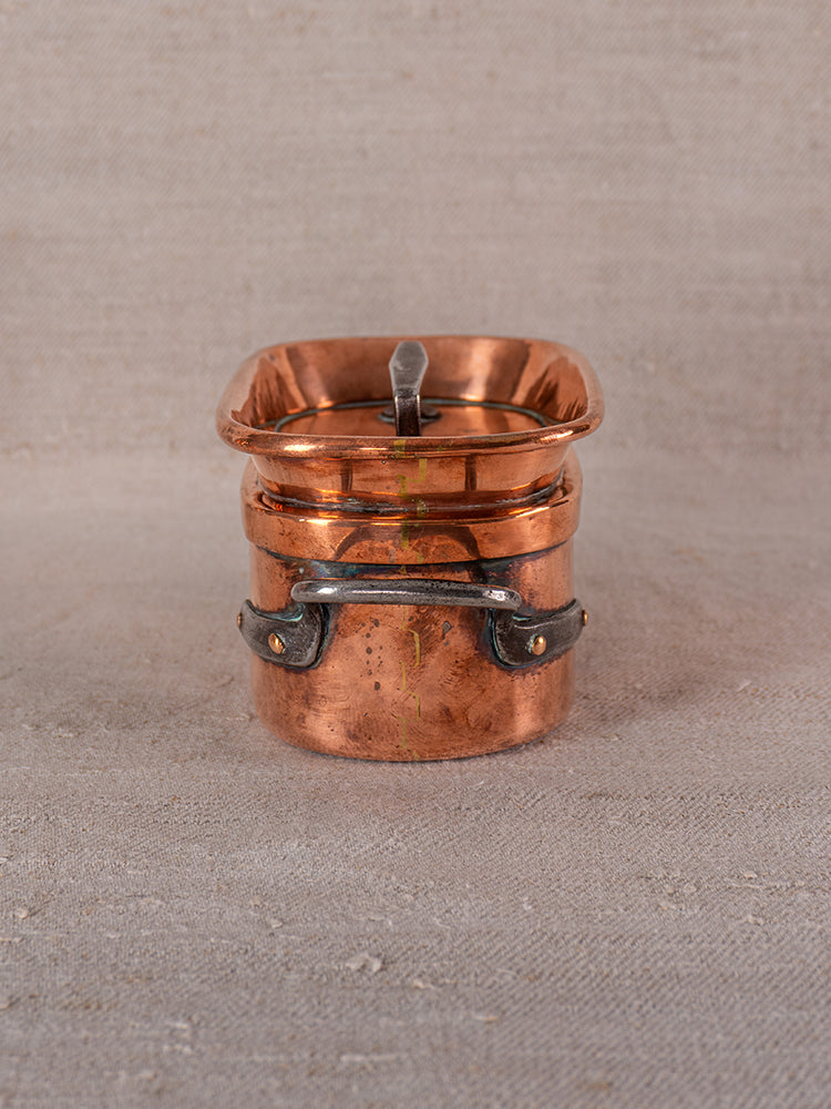 19th century French copper apprentice daubiere and saucepans with spoon on textured beige fabric.