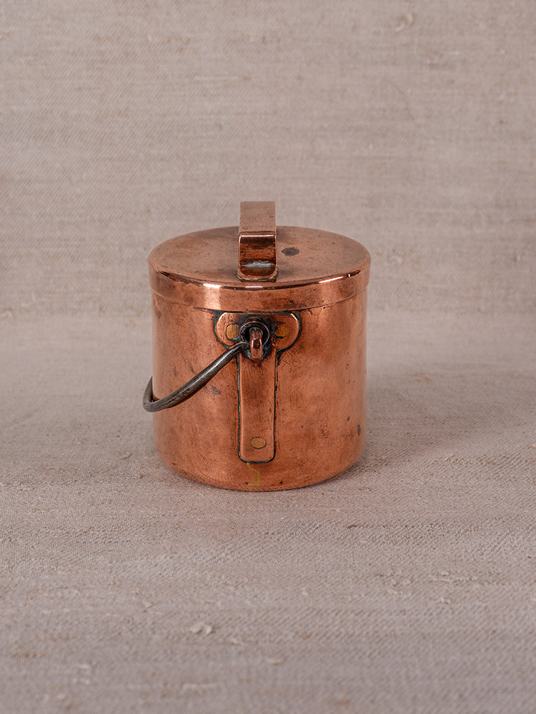 Antique French copper apprentice daubiere and saucepans set with lid and metal handle on beige fabric surface.
