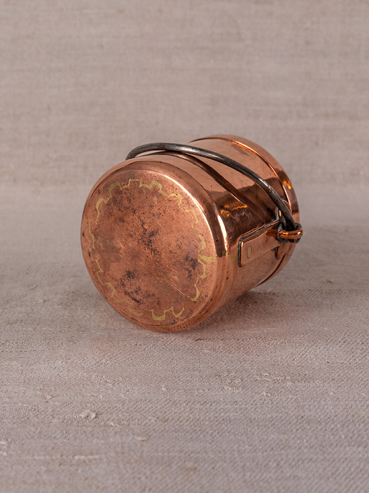 Antique French copper apprentice saucepan with metal handle, 19th-century patina and delicate edging on neutral surface.