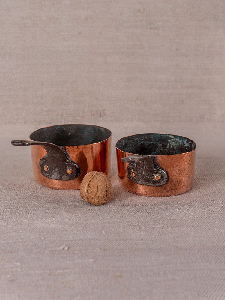 Antique French copper apprentice set with 19th-century daubiere and saucepans on beige fabric, walnut accent.