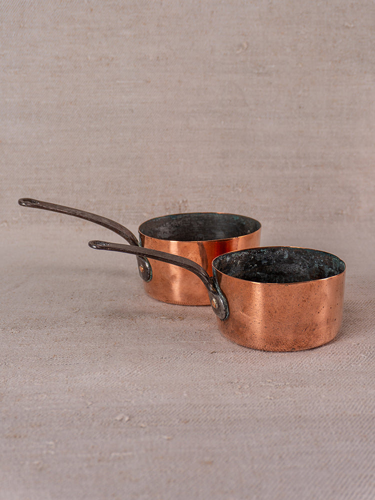 Antique French copper apprentice set with daubiere and 19th-century saucepans on a textured beige surface, aged patina visible.