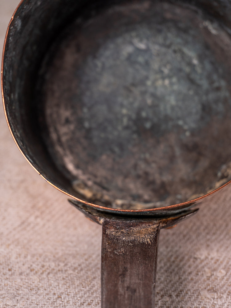 Antique French copper daubiere and saucepans with tarnished interiors and worn handles on textured beige fabric.