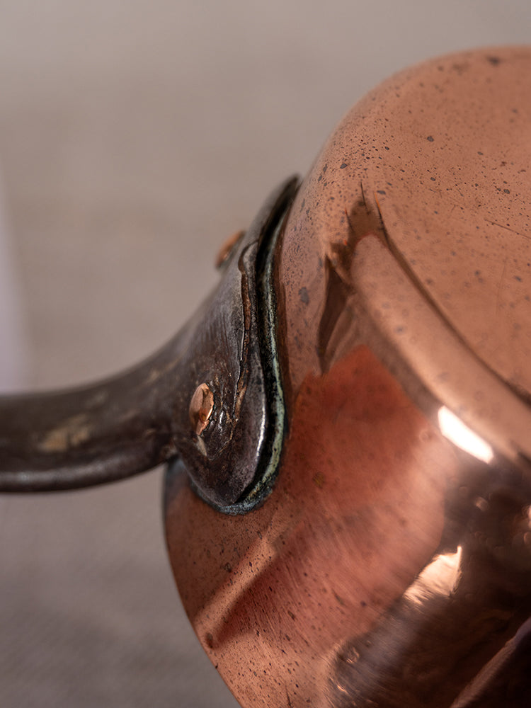 Antique French copper daubière handle joint with visible patina, oxidation near rivets, and tarnished, scratched surface.