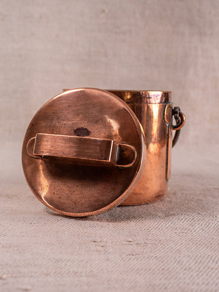 Antique French copper daubiere with handled lid and slight tarnish on beige textured fabric.