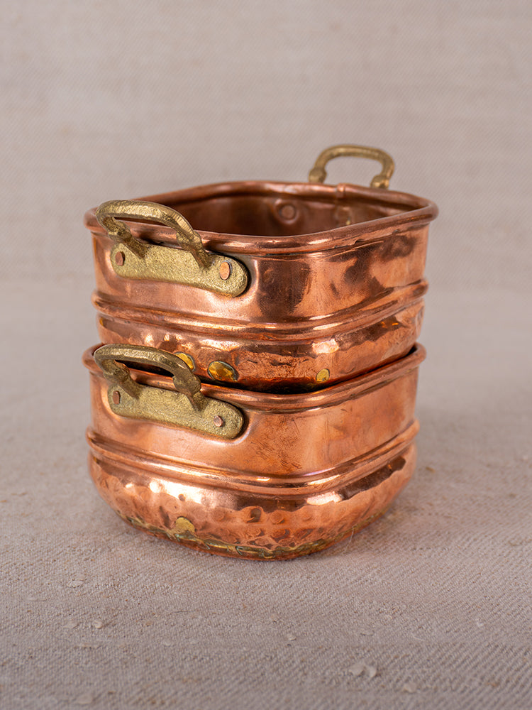 Pair of antique French hammered copper pots with brass handles, stacked on a neutral textured surface.