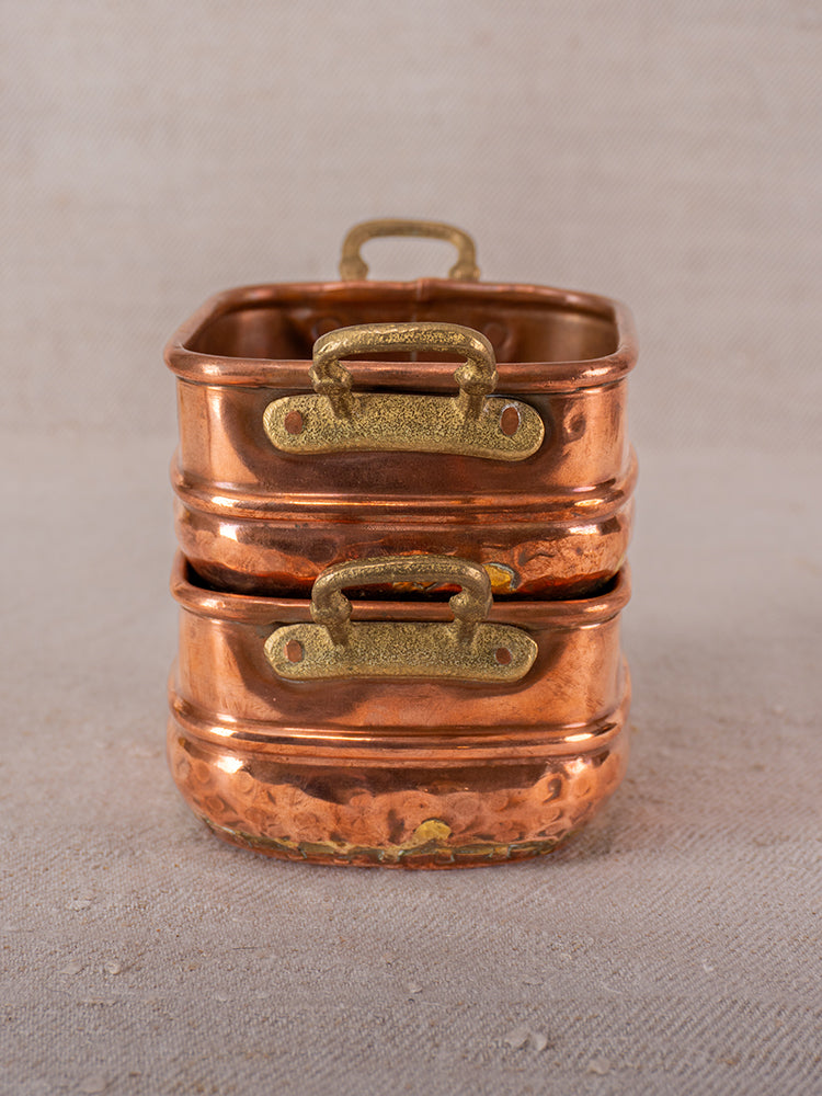 Pair of antique French hammered copper pots with brass handles, late 19th–early 20th century, on beige fabric.
