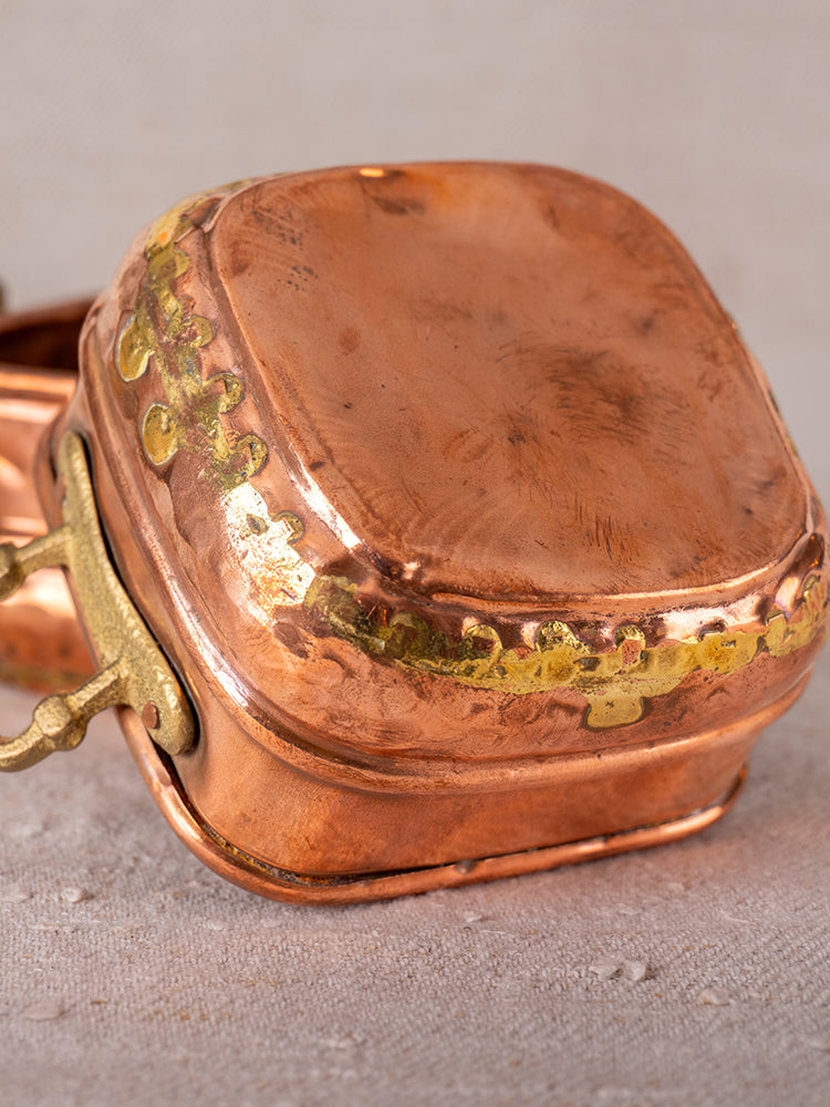 Pair of antique French hammered copper pots with brass handles and decorative seams on neutral fabric background.