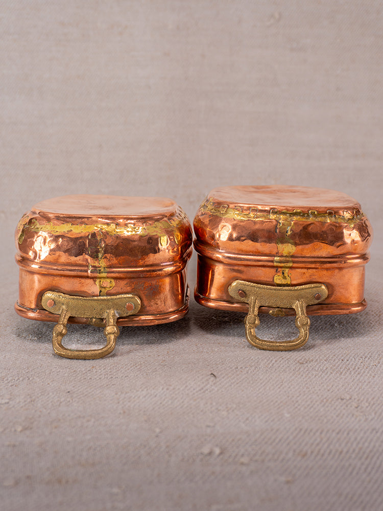 Pair of antique French hammered copper pots with brass handles and dovetail seams on beige textured surface.