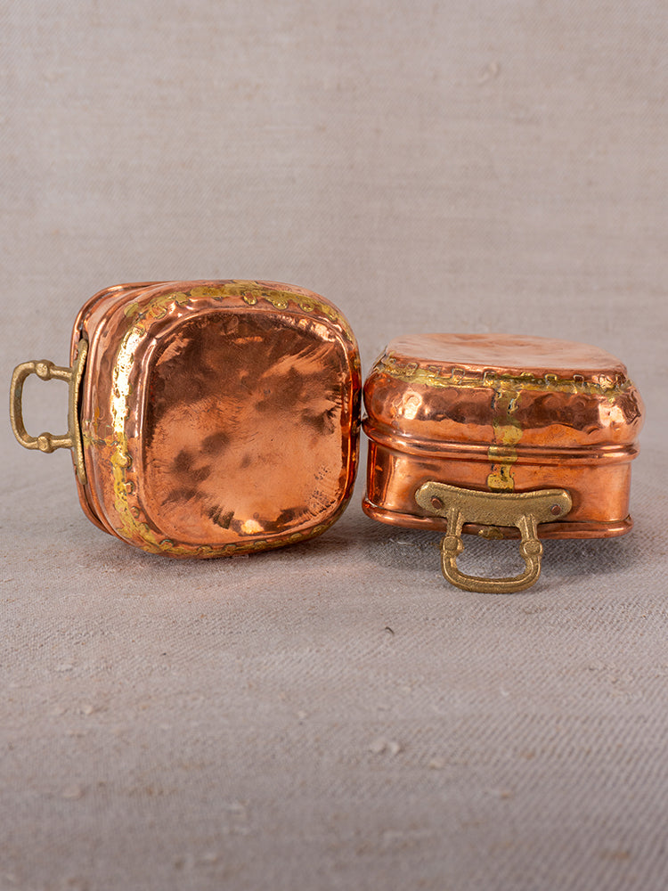 Pair of Antique French hammered copper pots with brass handles displayed on neutral fabric, one upright, one lidded.