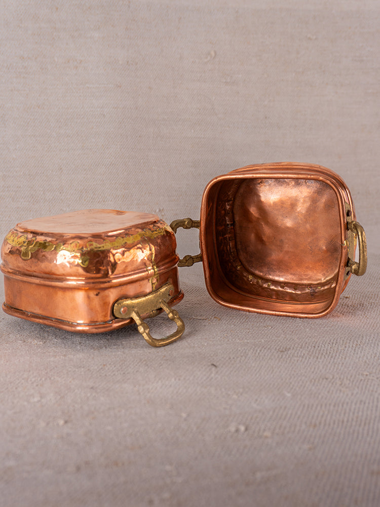 Pair of antique French hammered copper pots with brass handles, late 19th–early 20th century, on textured surface.
