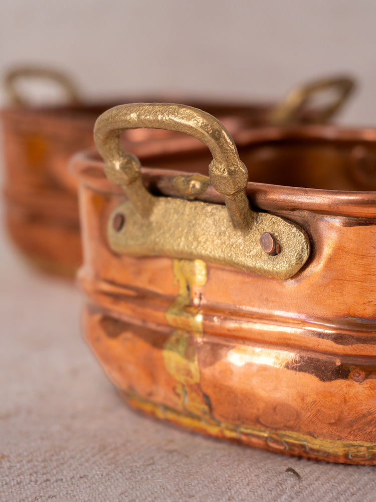 Antique French hammered copper pots with brass handles, one pot in sharp focus and another softly blurred behind.