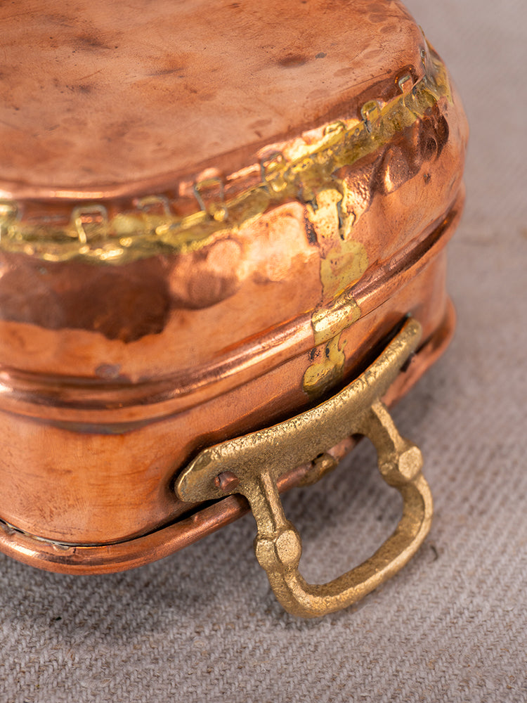Pair of antique French hammered copper pots with brass handles, late 19th to early 20th century, on beige fabric.