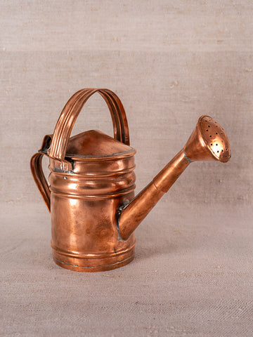 Antique French copper watering can with curved handle and long spout on a neutral fabric background.