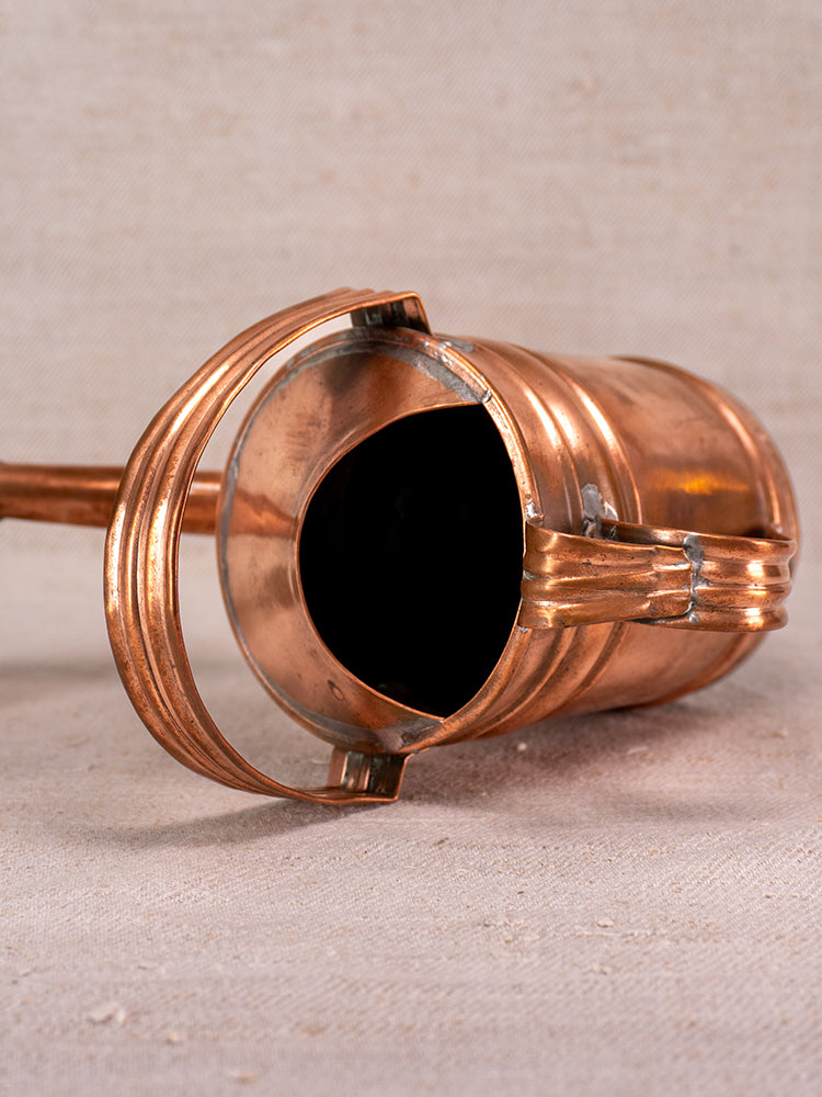 Antique French copper watering can with riveted details, open top, and curved handle on a light textured surface.