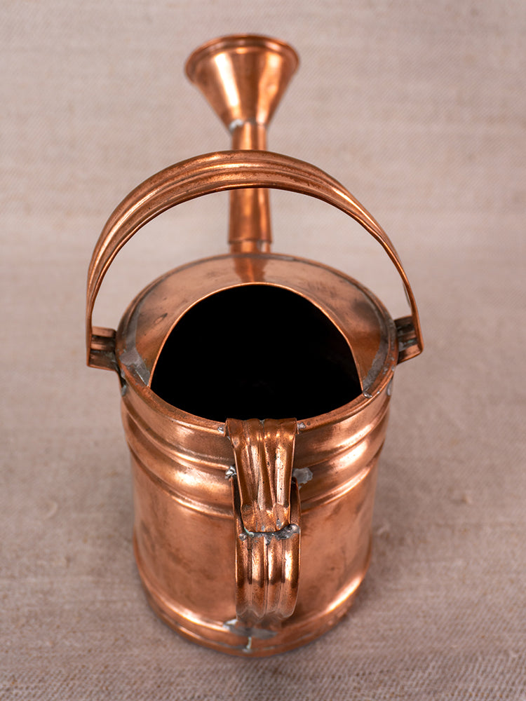 Antique French copper watering can with curved handle and wide spout, polished, on neutral fabric.