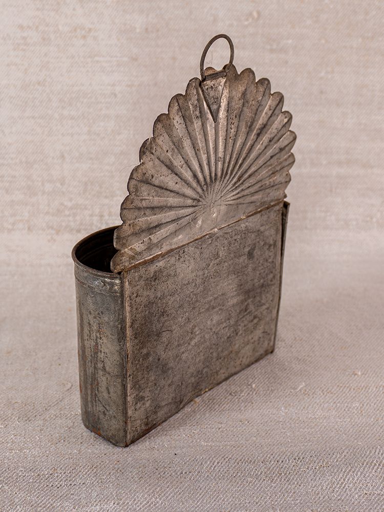 Provençal aged steel wall-mounted utensil holder with fan-shaped lid on neutral fabric background for vintage Luberon decor.
