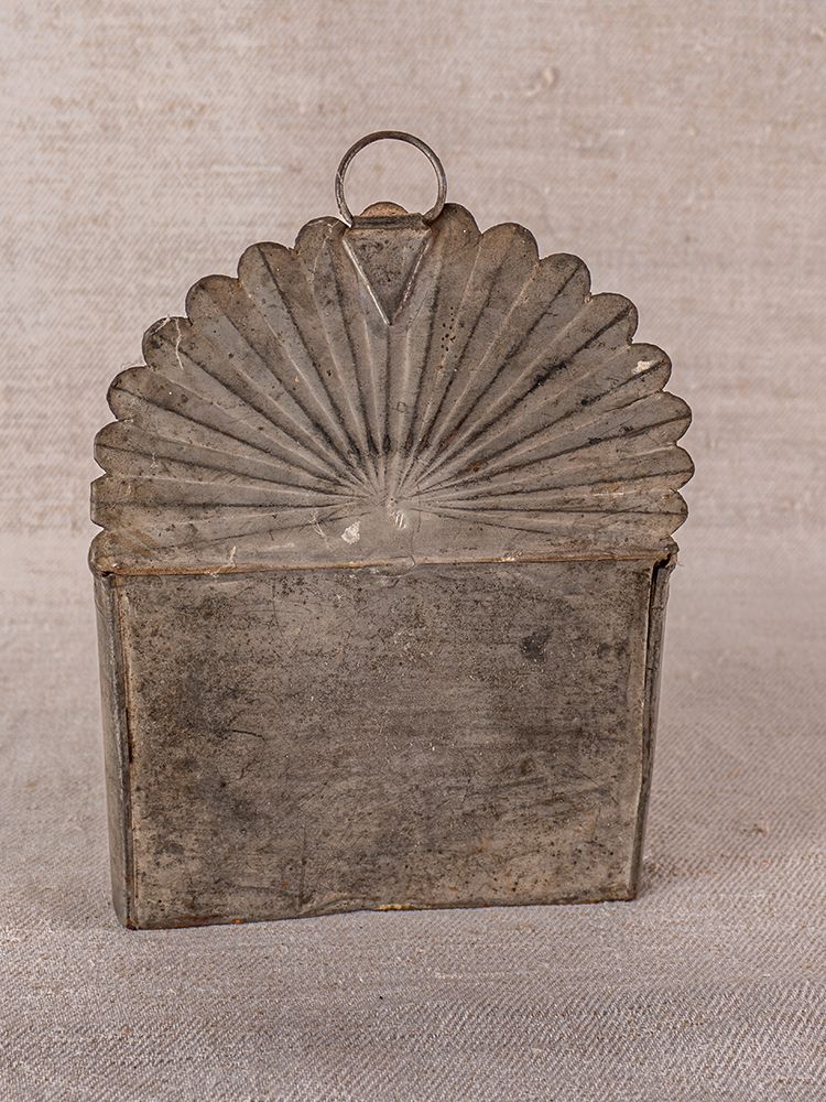 Vintage Provençal wall-mounted utensil holder in aged steel with scalloped top and hanging ring on neutral fabric backdrop.