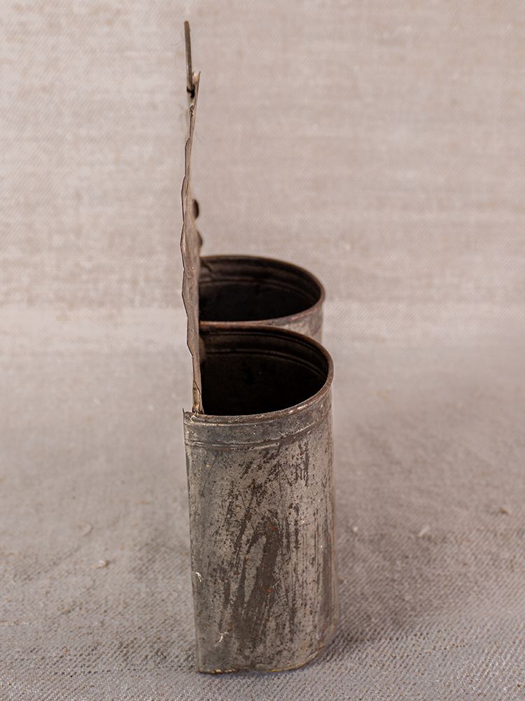 Provençal aged steel wall utensil holder with two cylindrical compartments, hinged back, French country style on textured surface.